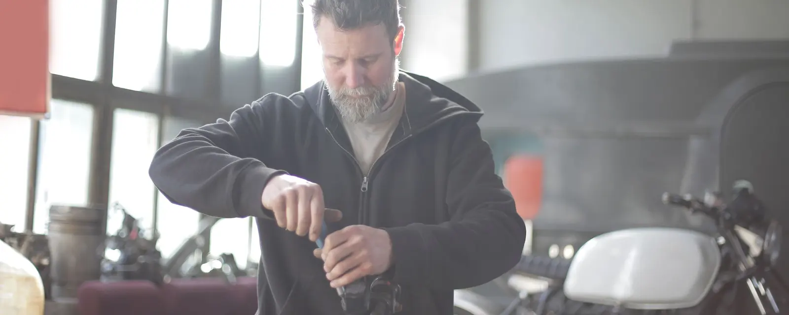A mechanic assembles a part beside a classic motorbike in a bright workshop